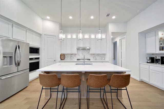 kitchen with white cabinets, appliances with stainless steel finishes, an island with sink, sink, and a breakfast bar