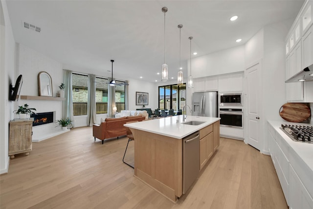 kitchen featuring white cabinetry, stainless steel appliances, a kitchen island with sink, pendant lighting, and sink