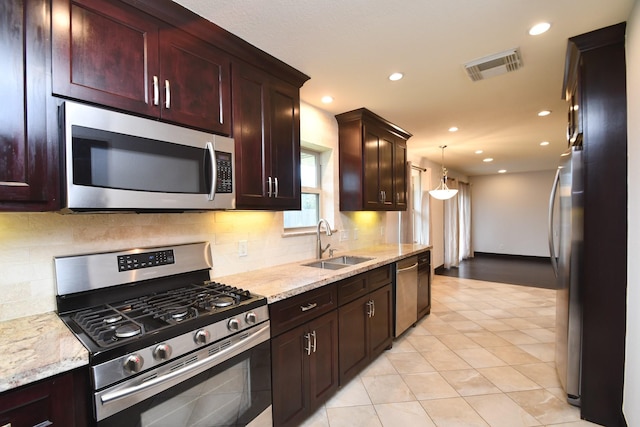 kitchen featuring pendant lighting, appliances with stainless steel finishes, sink, light stone counters, and light tile patterned floors