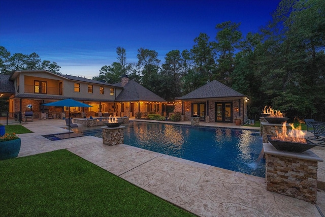 pool at dusk with an outdoor structure, an outdoor fire pit, pool water feature, and a patio