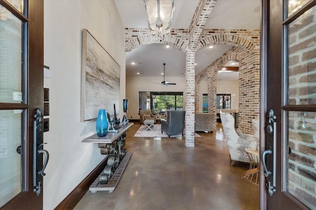 foyer with brick wall, concrete flooring, and ceiling fan with notable chandelier