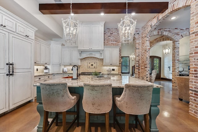 kitchen featuring a kitchen island with sink, white cabinets, decorative backsplash, and light stone countertops