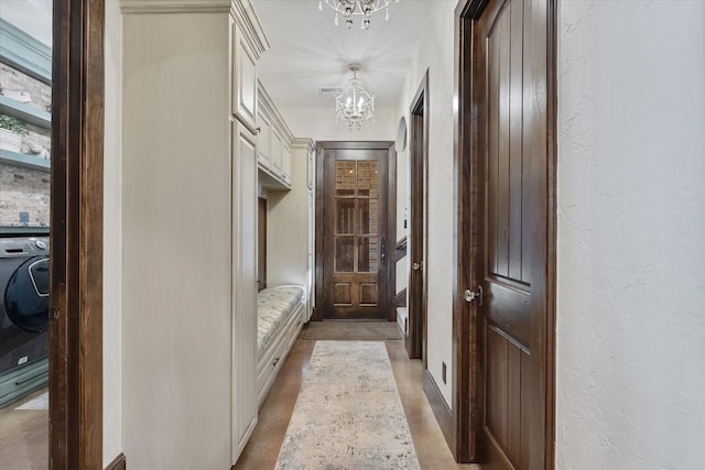 corridor with washer / clothes dryer and a chandelier