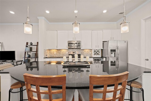 kitchen with white cabinetry, hanging light fixtures, a kitchen island with sink, and stainless steel appliances