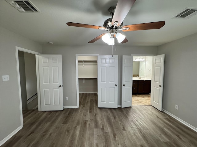 unfurnished bedroom with a spacious closet, connected bathroom, ceiling fan, a closet, and hardwood / wood-style flooring