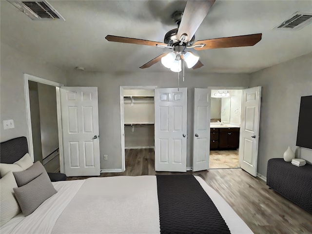 bedroom with ceiling fan, light wood-type flooring, connected bathroom, a walk in closet, and a closet