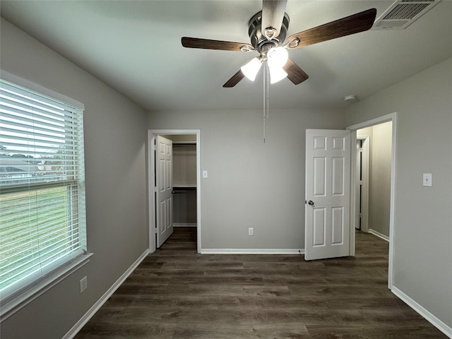 unfurnished bedroom featuring ceiling fan, a spacious closet, and dark wood-type flooring