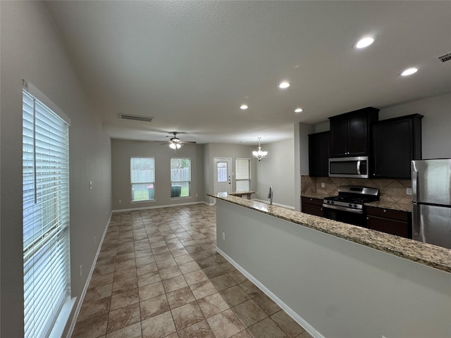 kitchen with stainless steel appliances, backsplash, hanging light fixtures, ceiling fan with notable chandelier, and light stone counters