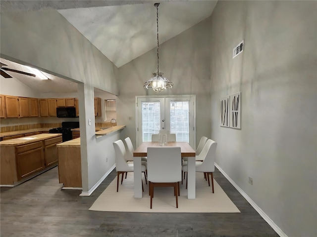 dining space featuring dark wood-type flooring, ceiling fan with notable chandelier, french doors, and high vaulted ceiling