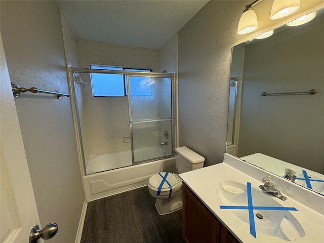 full bathroom featuring combined bath / shower with glass door, vanity, wood-type flooring, and toilet