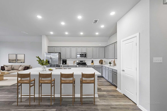 kitchen featuring stainless steel appliances, a kitchen breakfast bar, dark hardwood / wood-style floors, a kitchen island with sink, and gray cabinetry