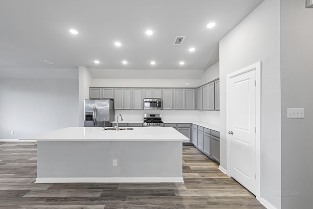 kitchen featuring appliances with stainless steel finishes, dark hardwood / wood-style flooring, an island with sink, sink, and gray cabinetry