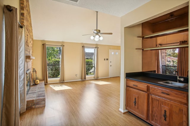 kitchen with a textured ceiling, a fireplace, sink, light wood-type flooring, and ceiling fan