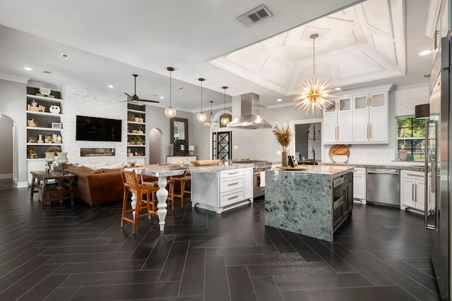 kitchen with island exhaust hood, high quality appliances, a center island with sink, and hanging light fixtures