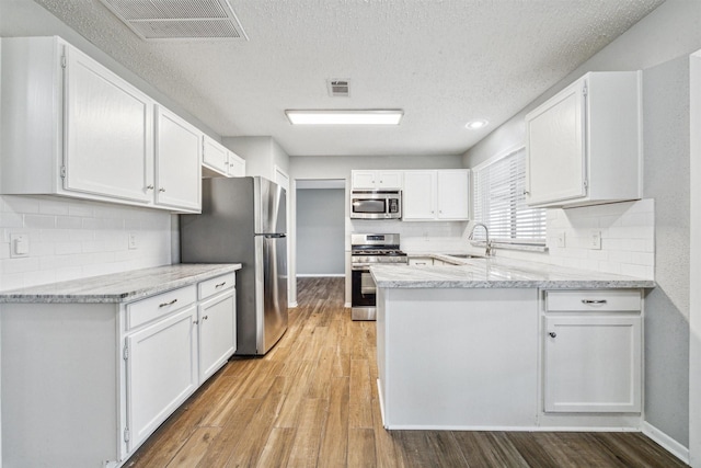 kitchen featuring light stone countertops, a textured ceiling, appliances with stainless steel finishes, white cabinetry, and sink