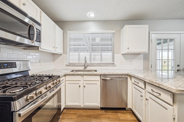 kitchen with sink, light stone countertops, appliances with stainless steel finishes, plenty of natural light, and white cabinets