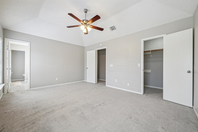 unfurnished bedroom featuring ceiling fan, ensuite bathroom, vaulted ceiling, a textured ceiling, and light carpet