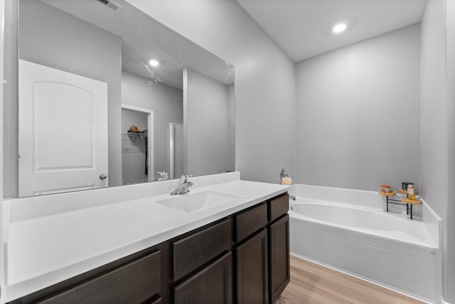 bathroom featuring hardwood / wood-style flooring, tiled tub, and vanity