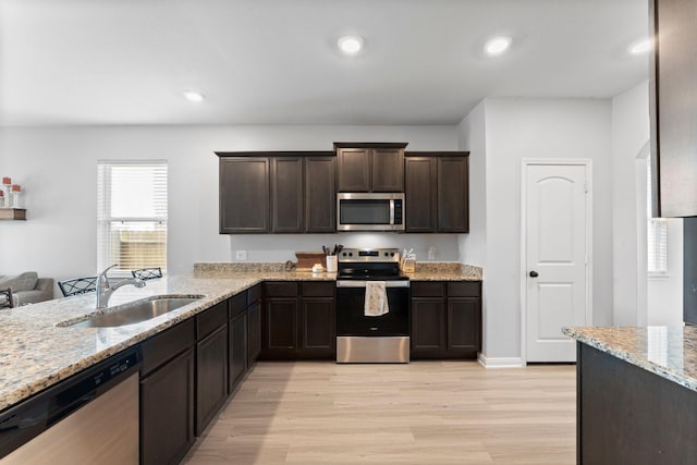 kitchen with light wood-type flooring, appliances with stainless steel finishes, sink, and light stone counters