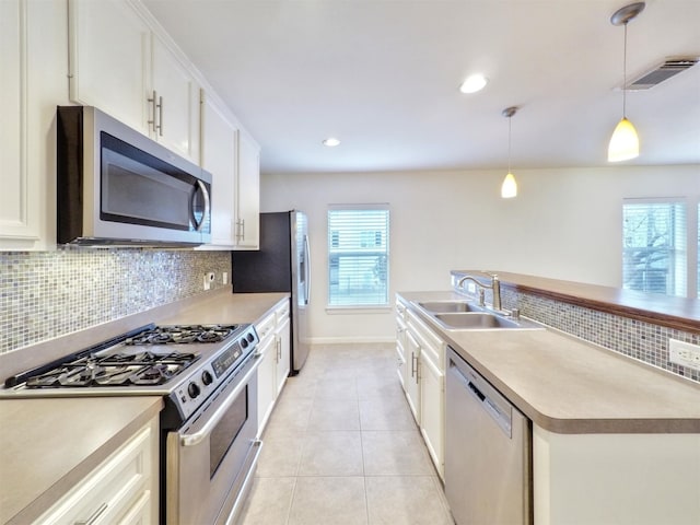 kitchen with hanging light fixtures, sink, stainless steel appliances, and white cabinetry