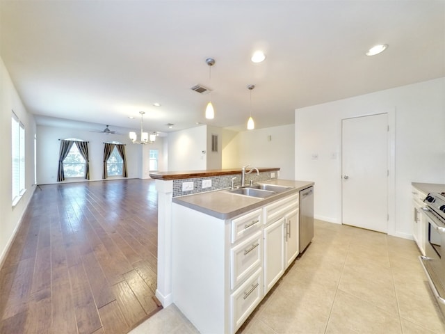 kitchen with decorative light fixtures, white cabinets, a kitchen island with sink, and sink