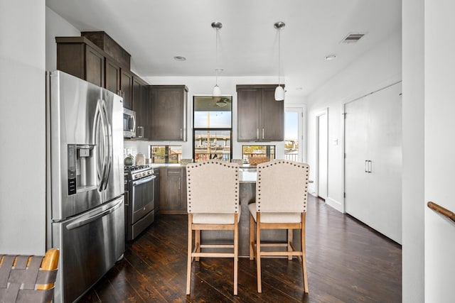 kitchen with appliances with stainless steel finishes, a center island, decorative light fixtures, dark wood-type flooring, and dark brown cabinets