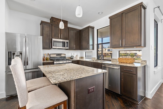 kitchen with decorative light fixtures, dark hardwood / wood-style floors, a center island, stainless steel appliances, and light stone counters