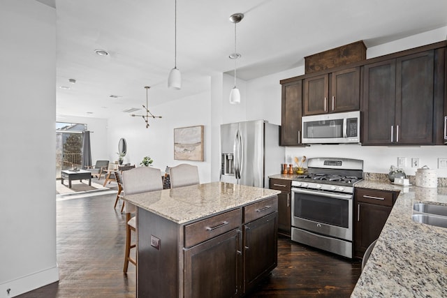 kitchen with stainless steel appliances, decorative light fixtures, a kitchen breakfast bar, dark brown cabinets, and a center island