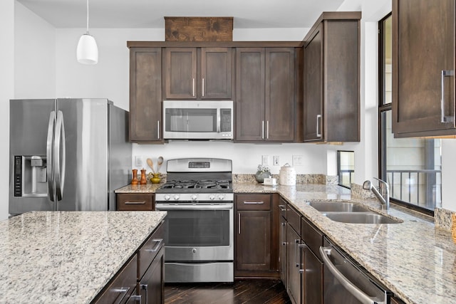 kitchen featuring appliances with stainless steel finishes, pendant lighting, light stone counters, dark brown cabinetry, and sink