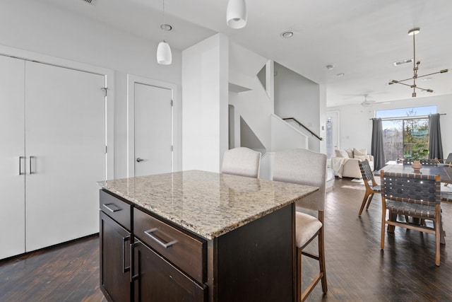 kitchen with a center island, decorative light fixtures, dark wood-type flooring, a kitchen breakfast bar, and light stone counters