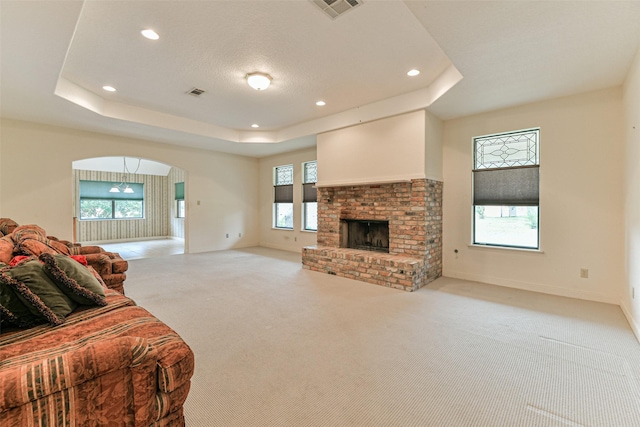 carpeted living room featuring a raised ceiling and a brick fireplace