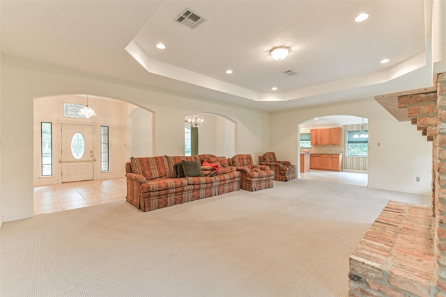 carpeted living room with a tray ceiling and a chandelier