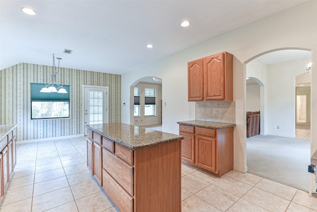 kitchen with a kitchen island, dark stone countertops, light colored carpet, and decorative light fixtures