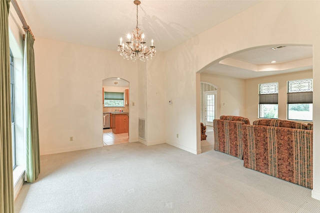 empty room featuring light colored carpet, a raised ceiling, and a notable chandelier