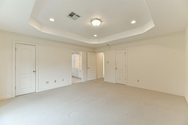 unfurnished bedroom featuring ensuite bathroom, light colored carpet, and a tray ceiling