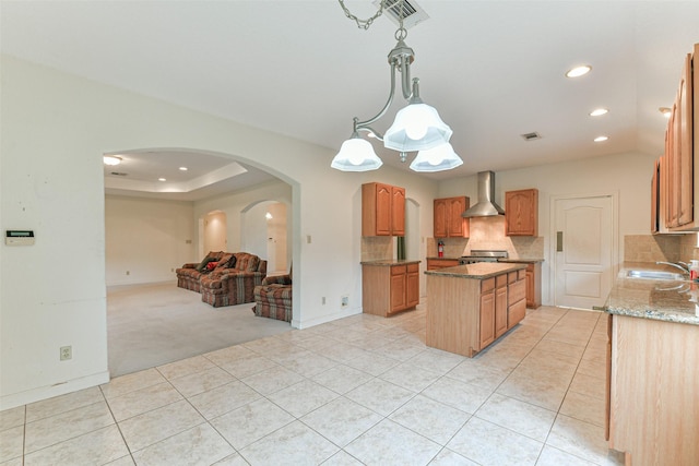 kitchen featuring hanging light fixtures, light tile patterned flooring, wall chimney range hood, and a kitchen island