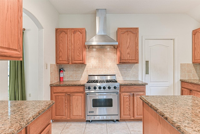 kitchen with light stone counters, wall chimney exhaust hood, premium stove, and tasteful backsplash