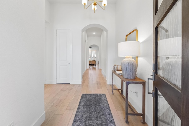 hall with a notable chandelier, a towering ceiling, and light hardwood / wood-style flooring