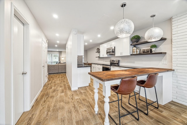 kitchen featuring pendant lighting, white cabinetry, stainless steel appliances, light wood-type flooring, and butcher block countertops