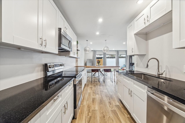 kitchen with appliances with stainless steel finishes, sink, white cabinetry, and light hardwood / wood-style flooring