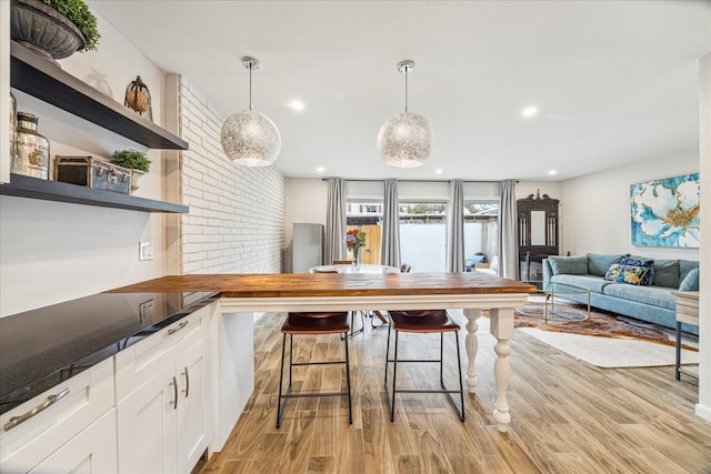 kitchen featuring a kitchen bar, hanging light fixtures, white cabinets, and light wood-type flooring