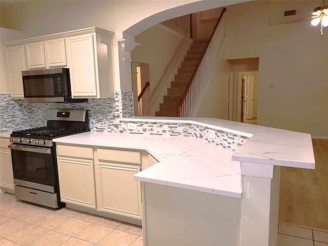 kitchen with light tile patterned floors, kitchen peninsula, appliances with stainless steel finishes, and white cabinetry