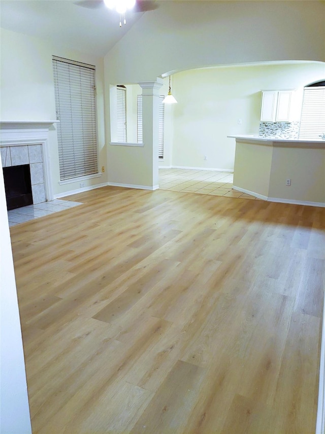 unfurnished living room featuring vaulted ceiling, ceiling fan, light hardwood / wood-style flooring, and a tiled fireplace