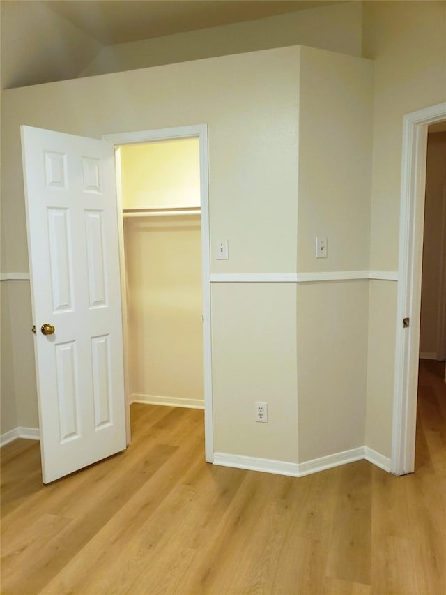 unfurnished bedroom with light wood-type flooring, a closet, and vaulted ceiling