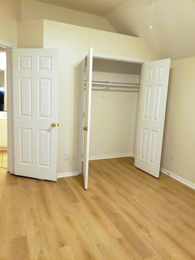 unfurnished bedroom with vaulted ceiling, a closet, and light wood-type flooring