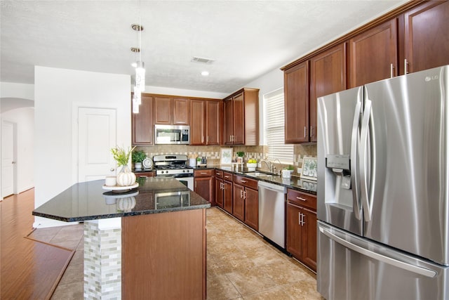 kitchen featuring a kitchen island, stainless steel appliances, dark stone counters, sink, and hanging light fixtures