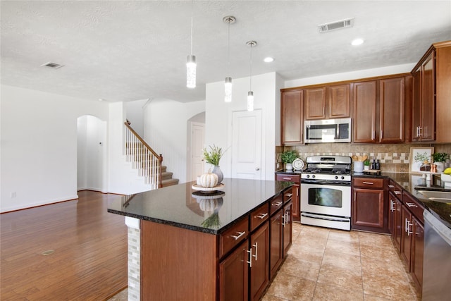 kitchen featuring decorative light fixtures, dark stone counters, stainless steel appliances, and a kitchen island