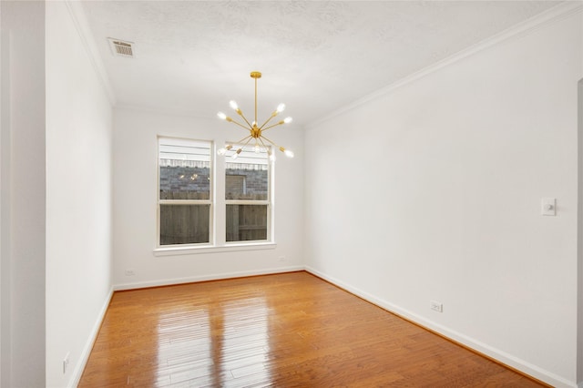 spare room with wood-type flooring, ornamental molding, and a notable chandelier