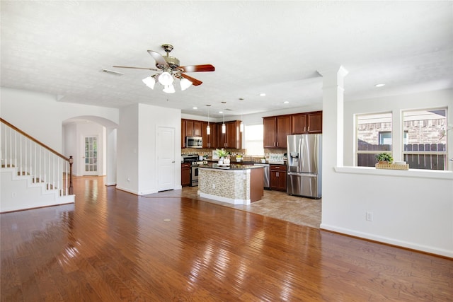 kitchen with stainless steel appliances, decorative backsplash, a kitchen island, a wealth of natural light, and pendant lighting