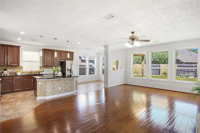 kitchen with stainless steel refrigerator with ice dispenser, backsplash, decorative light fixtures, a kitchen island, and sink